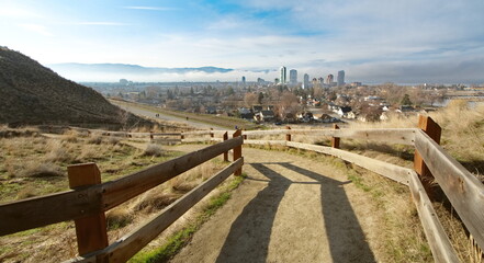View down a mountain pathway overlooking a city, as bright sunlight crests the mountain, making crisp shadows on the ground.