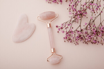 Face roller and gua sha massager on a pink background with gypsophila. Self facial massage concept