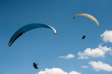 Two paragliders flying in the blue sky against the background of clouds. Paragliding in the sky on a sunny day.