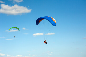 Two paragliders flying in the blue sky against the background of clouds. Paragliding in the sky on a sunny day.