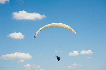 Alone white paraglider flying in the blue sky against the background of clouds. Paragliding in the sky on a sunny day.