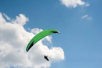 Alone green paraglider flying in the blue sky against the background of clouds. Paragliding in the sky on a sunny day.