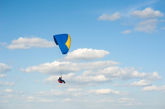 Alone blue and yellow paraglider flying in the blue sky against the background of clouds. Paragliding in the sky on a sunny day.