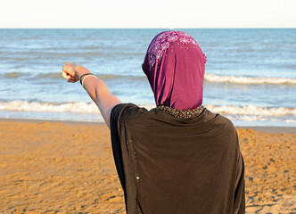woman with veil and typical Arab clothes indicates with her hand a place in the sea