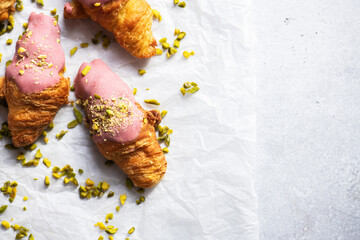 Mini-croissants with ruby chocolate and pistachios on a baking paper, gray background. Top view and copy space. - 495991026