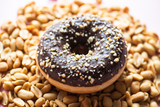 Doughnut with chocolate glaze and peanuts on a pink background. Top view.