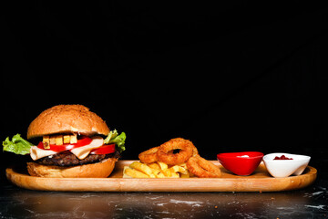 Hamburger with french fries, onion rings and sauces on wooden tray