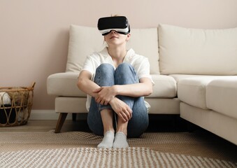 Fototapeta premium Testing new technologies. Attractive young woman in VR headset gesturing and smiling while sitting at home