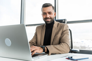 Businessman working on a laptop in the office and looking at the camera with a smile