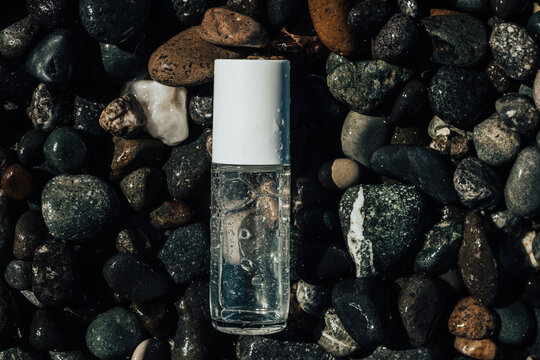 Flat lay composition of a beauty product transparent bottle on wet beach stones . Fresh ocean scented product mock up. 