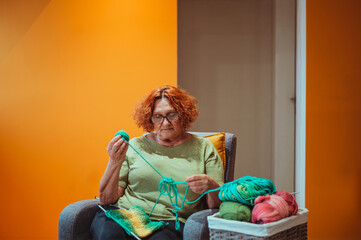 Mature woman holding knitting needles and knitting at home.