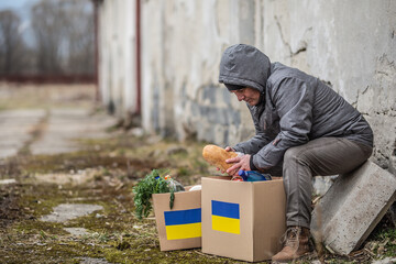 Older man takes bread out of box full of humanitarian aid for Ukraine in the war-torn area