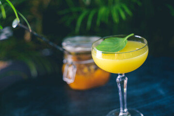 Kumquat basil martini cocktail served on the black countertop. The yellow tasty drink served in martini glass by proffesional bartender.