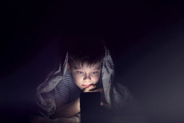 boy under the covers with a phone at night. gadget addicted children. teenager man use mobile phone...
