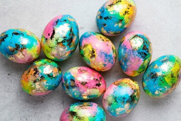 Happy Easter holiday greeting card with gold, blue, yellow, pink painted speckled easter eggs on grey background. Top view.