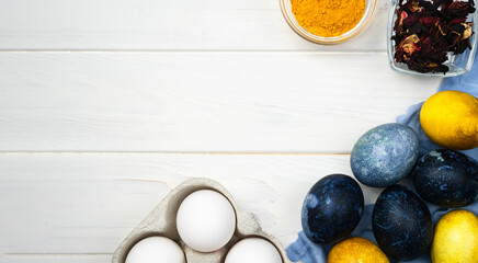 Banner. Easter flatlay composition with painted blue and yellow Easter eggs and natural food coloring on a wooden white background. Top view. Place for text.