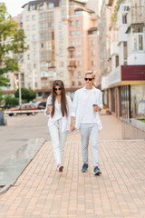 guy with a girl in white clothes walks around the city and drinks coffee