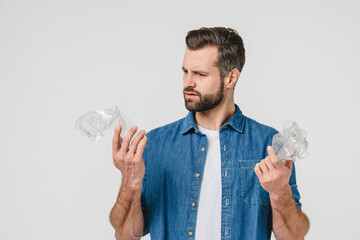 Disappointed caucasian young eco-activist volunteer holding plastic bottles for recycling, protecting nature environment against pollution isolated in white background