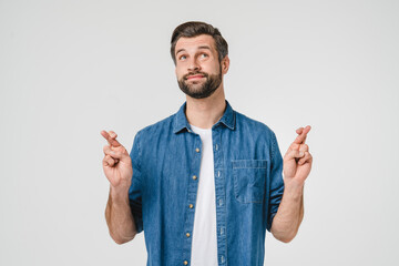 Caucasian superstitious young man in casual clothes crossing his fingers for good luck in bet...
