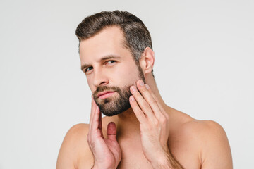 Aftershave cosmetics. Caucasian young naked shirtless man preparing for shaving with razor touching his beard isolated in white background - obrazy, fototapety, plakaty