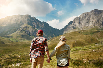 Reaching new heights as a couple. Rearview shot of a young couple admiring a mountainous view in...