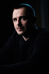 Profile portrait of a concentrated guy in a black jacket, in a dark room. Serious look. Blue eyes