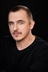 Fototapeta premium Portrait of a cold-blooded guy in a black jacket, who is looking at the camera. Blue eyes