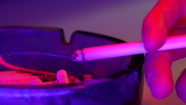 Close up shot of cigarette on table. Neon light on disco, party time and person is smoking a lot of. Bad habit, relaxation and cancer risk.