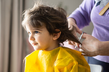 Little cute boy is sitting and having a haircut by his grandmother 