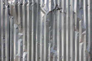 Old galvanized fence with dents and side lighting.