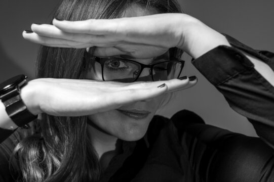 Black and white photo, close up portrait of a cheerful girl in glasses showing happiness, smiling. She covers her face with her hand so that she pierces it. Place for copy in