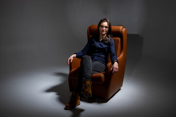 Beautiful, young, emotional, tired and frustrated woman sitting on a brown leather chair in a...