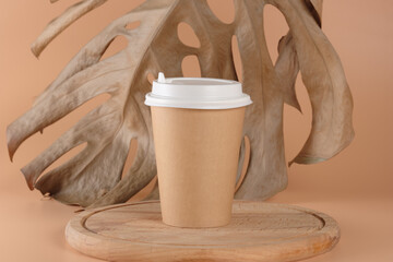 A cardboard cup for hot drinks, tea or coffee on a wooden podium or tray. In the background is a...