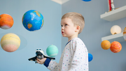 Portrait boy is playing with toy space shuttle, flying in space among planets of solar system. Child playing at home with space shuttle flying in space of solar system. Cosmonautics Day on April 12.