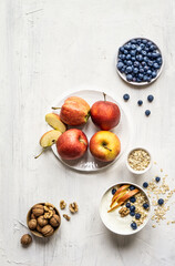 Top view of healthy muesli with oat flakes fruits and walnut over gray background. In a middle is apple, on top is blueberry on plate and at the bottom of the photo are walnuts and flakes.