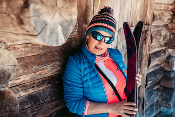 Kobieta szczęśliwa z nartami w zimowy dzień pozuje przy starej stodole. - obrazy, fototapety, plakaty