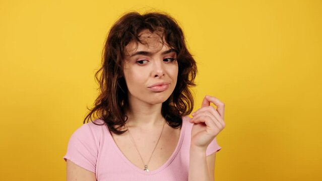 Young woman thoughtfully pondering on camera and shrugs. Attractive young girl on yellow background. High quality 4k footage