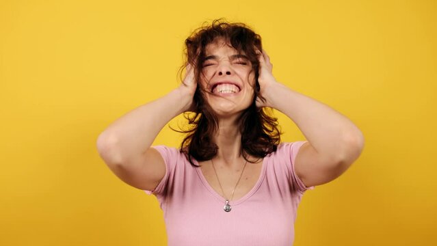 Woman screaming clutching hands over head with frightened face. Attractive young girl on yellow background. High quality 4k footage