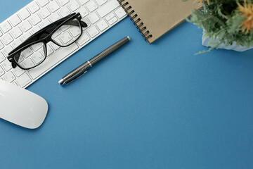 Keyboard mouse phone pen notebook glasses on blue background