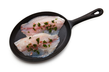 White fish fillet spilled with salt and chopped parsley lies on a cast-iron pan