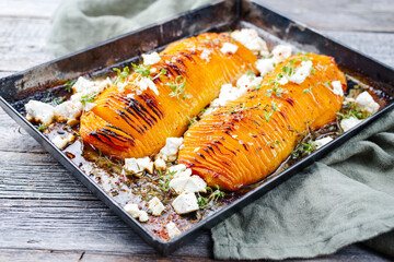 Traditional fried Hasselback butternut squash pumpkin roast with herbs and feta sheep cheese served as close-up in a rustic metal tray on a wooden board