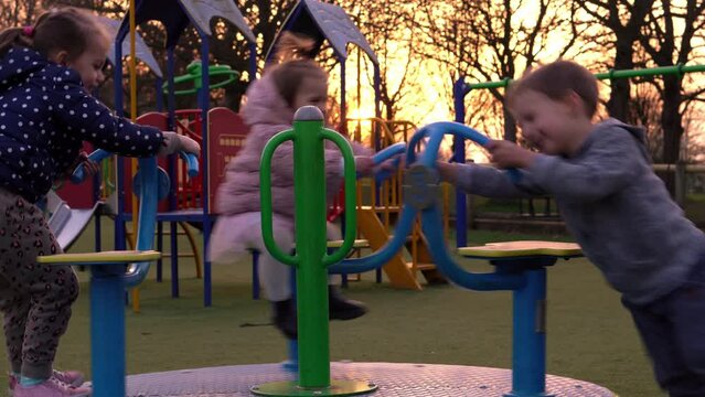 Three little Happy Children having fun spinning on merry-go-round. Smiling Siblings friends playing outside. emotional kids rides on carousel at playground nursery in park.Happy family, childhood
