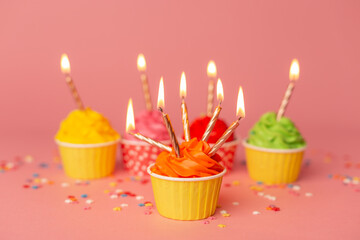 A colorful birthday cupcakes with candle on the pink background. Birthday cupcakes