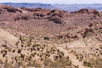 Nelson, Nevada, USA - May 21, 2011: Rough beige-brown terrain with short cacti and other plants growing in the valleys between mountains. Long view on table mountain and more.