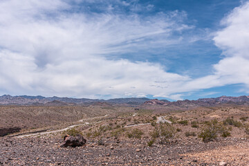 Nelson, Nevada, USA - May 21, 2011: Wide brown desert landscape with green bushes under blue cloudscape and route 165 winding through it.