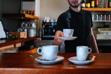 detail of a bar with two coffee cups. Waiter serving cups of coffee at the bar counter. Cups of coffee steaming.