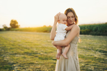 Fototapeta na wymiar Loving mother and baby at sunset. Beautiful woman and small child in nature background. Concept of natural motherhood. Happy healthy family at summer outdoors. Positive human emotions and feelings.