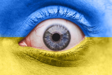 Naklejka premium Concept against military action. The eye of a frightened person on the face in the colors of the Ukrainian flag. Close-up. Selective focus.