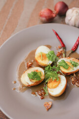 Egg with Tamarind Sauce in a white plate served on a wooden table with coriander sprinkles, is a popular local dish that Thai people eat.