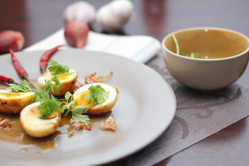 Egg with Tamarind Sauce in a white plate served on a wooden table with coriander sprinkles, is a popular local dish that Thai people eat.